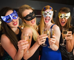 Attractive friends with masks on holding champagne glasses laughing at camera